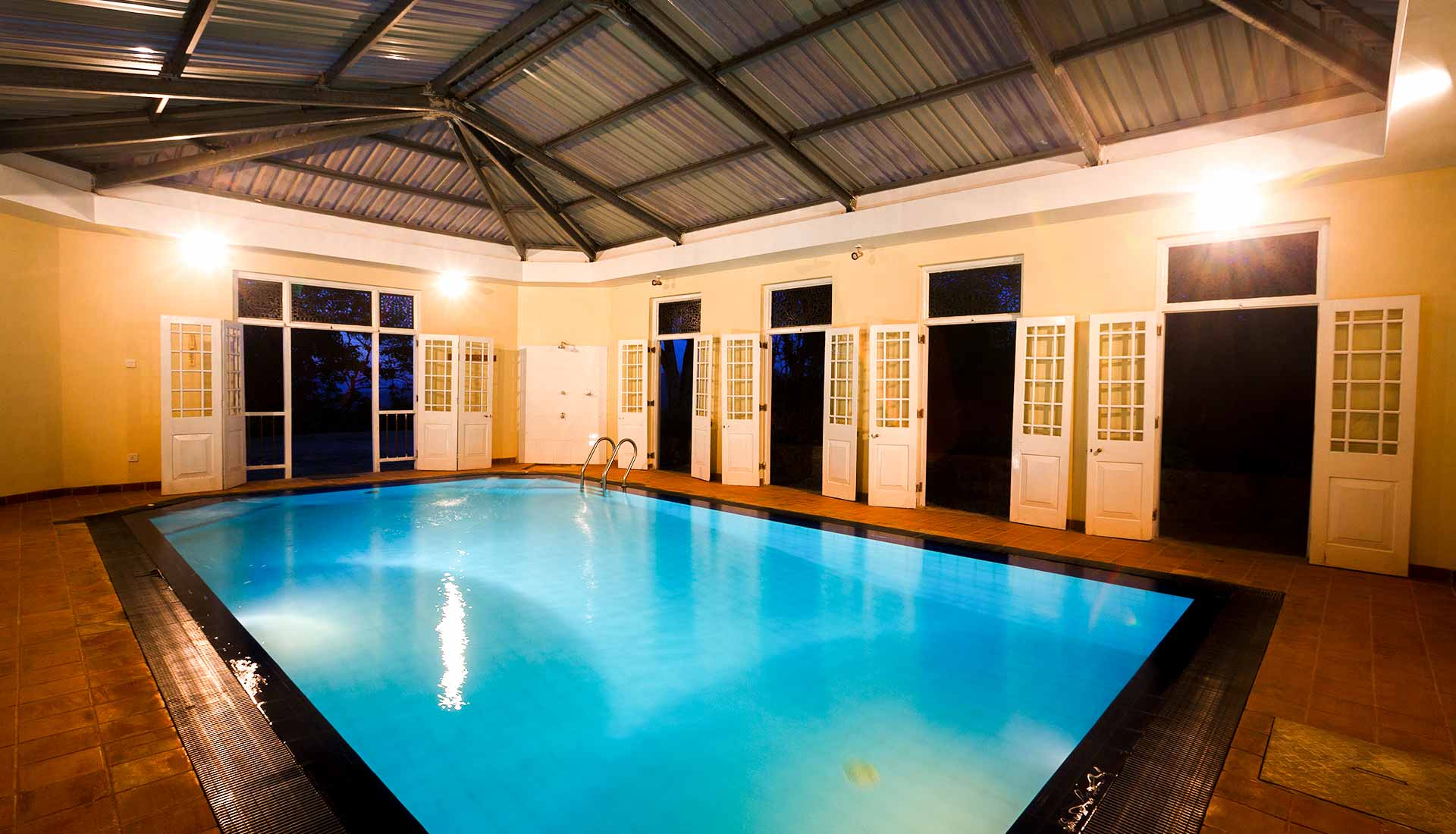 The indoor swimming pool under a pitched timber roof, lined with French doors